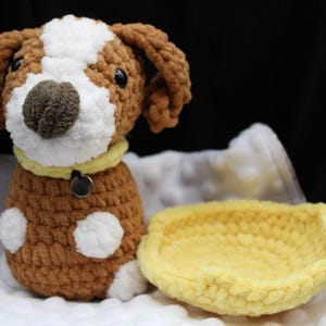 May include: A handmade crochet dog with brown and white fur, a yellow collar, and a small tag. Beside the dog is a matching yellow crochet pet bed. The dog has black eyes and a brown nose. The dog has white spots on its body.