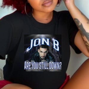 May include: Black t-shirt with a graphic of Jon B, a rapper, with the text "Are you still down?" in white letters.
