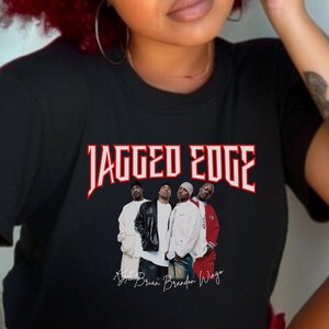 Puede incluir: Camiseta negra con un gráfico rojo y blanco de la banda Jagged Edge. El gráfico incluye el nombre de la banda y una foto de los cuatro miembros. El texto "Kyle Brian Brandon Wingo" está escrito en blanco debajo del gráfico.
