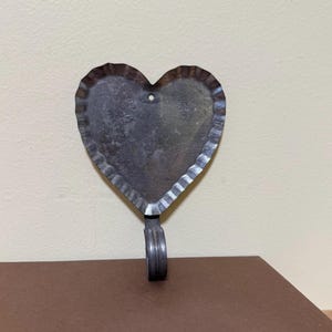 May include: A metal heart-shaped hook with a scalloped edge. The hook is silver in color and has a simple design.
