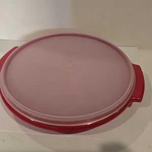 May include: A round, red and pink food storage container with a lid. The container has a red base and handles, and a pink lid. The lid has a slightly translucent appearance. The container is designed for food storage.