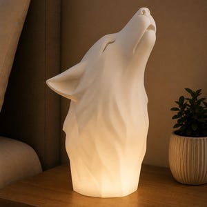 Pode incluir: Uma lâmpada branca mate com design geométrico em forma de cabeça de lobo a uivar. A escultura apresenta superfícies facetadas e angulares, emitindo um brilho interno suave e quente a partir da base, iluminando o pescoço e o focinho do lobo.