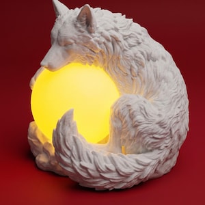 Può includere: Una statuetta di lupo bianco raggomitolata in forma circolare, caratterizzata da una texture del pelo dettagliata e da una fonte di luce sferica gialla luminosa tenuta all'interno del corpo. La scultura ha una finitura opaca e una luce calda.