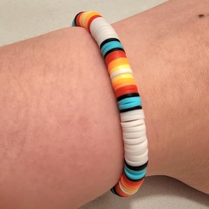 Op de afbeelding: Een kleurrijke kralen armband met witte, oranje, rode, zwarte en blauwe kralen. De armband is gemaakt van ronde, platte kralen.