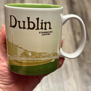 May include: White ceramic mug with the word "Dublin" in brown lettering. The mug features a green interior and a scenic illustration of Dublin, Ireland, with the Starbucks Coffee logo.