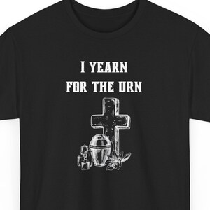 May include: Black t-shirt with white text that reads "I yearn for the urn". The text is above a white image of a cross, an urn, and candles.