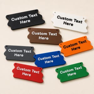 May include: A collection of eight rectangular tags with wavy edges, each featuring two small holes at the top corners. The tags come in black, white, brown, orange, dark gray, blue, red, and green, all displaying the text Custom Text Here.