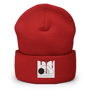 May include: A bright red cuffed beanie featuring a square patch on the front. The patch displays a black circular tomb entrance graphic with red liquid dripping from the top, set against a white background with the text 2 Corinthians 5:17 below.