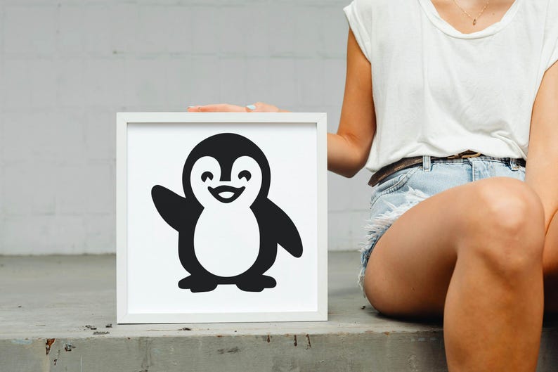 May include: A framed, black and white illustration of a cartoon penguin waving. The penguin has a white belly and a smiling face. The frame is white and square. The image is held by a person.