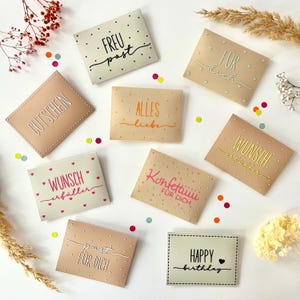 May include: A collection of beige and off-white gift cards with various handwritten phrases in different colors. Some cards have text like "FREU post", "GUTSCHEIN", and "HAPPY birthday". The cards are decorated with small dots and hearts.