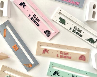 May include: A collection of colourful rectangular rulers, each with unique designs and the phrases "ENDLICH SCHULKIND!" and "Du bist 1. Klasse." The rulers feature ABCs, pencils, and rainbows. Ideal for a back-to-school theme.