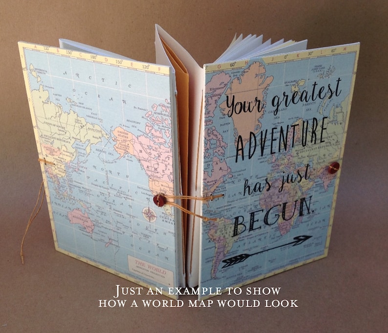 May include: A blue and white world map journal with the text "Your greatest adventure has just begun." printed on the cover. The journal is bound with brown twine and has a brown arrow pointing to the right.