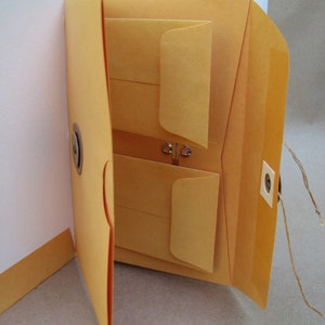 May include: A brown leather-bound journal with multiple pockets and flaps. The journal has a clasp closure and a brown leather strap.