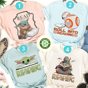 May include: Four different t-shirts featuring Star Wars characters reading books. The shirts are light pink, light blue, light blue, and cream. The text on the shirts reads "Read This is the Way", "Roll into Reading", "Reading is the Way", and "Reading is the Way".