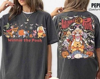 Op de afbeelding: Donkergrijs T-shirt met een Halloween-thema Winnie the Pooh ontwerp. De voorkant toont "Winnie the Pooh" met karakters als Tijger, Iejoor en Knorretje. De achterkant heeft een grotere illustratie met pompoenen en geesten.