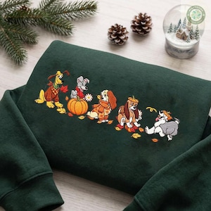 May include: A dark green sweatshirt featuring an embroidered design of five cartoon dogs in autumn attire. The dogs are depicted with a large orange pumpkin, scattered fall leaves, and small floral accents, creating a seasonal scene across the chest.