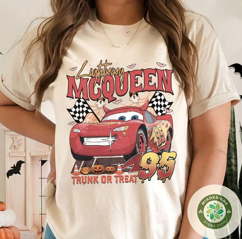 May include: Beige t-shirt featuring a graphic of Lightning McQueen from the movie Cars, with the text "Lightning McQueen" and "95". The design includes checkered flags, pumpkins, and the phrase "Trunk or Treat".
