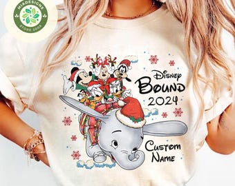 Puede incluir: Camiseta color crema con un diseño festivo de Disney. El gráfico incluye a Dumbo el elefante, Mickey Mouse, el Pato Donald y otros personajes, todos con gorros de Papá Noel. El texto dice "Disney Bound 2024" y "Custom Name".