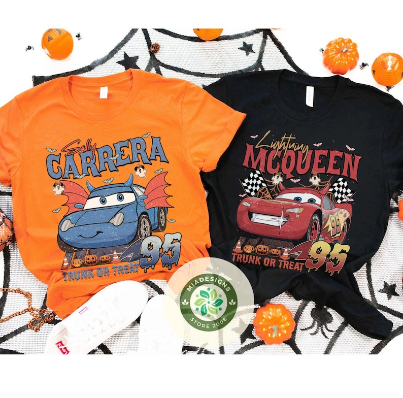May include: Two Halloween-themed t-shirts. One is orange with a blue car graphic and the text "Sally Carrera". The other is black with a red car graphic and the text "Lightning McQueen". Both shirts have "95" and "Trunk or Treat".