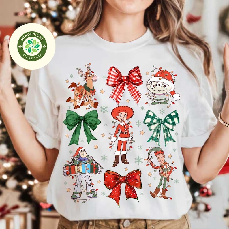 May include: White t-shirt featuring Christmas-themed cartoon characters and bows. The design includes characters like Buzz Lightyear and Little Green Men, with festive bows in red and green. The shirt has a round neck.