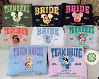 Op de afbeelding: Set van tien lichtgekleurde sweatshirts met verschillende Disney-prinsessenontwerpen. Elk sweatshirt heeft een prinsessenfiguur, een Mickey Mouse-orenontwerp en de tekst "Team Bride" of "Bride".