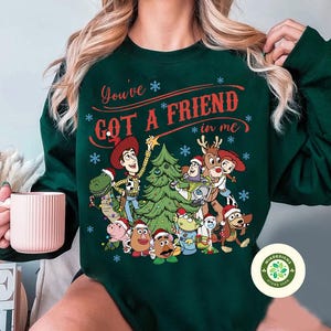 May include: Dark green sweatshirt featuring a festive design with characters from the Toy Story movie. The text "You've Got a Friend in Me" is displayed above the characters. The design includes a Christmas tree and snowflakes.