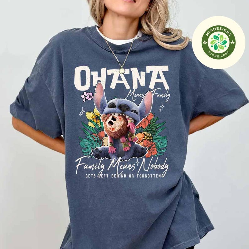 May include: A blue-grey t-shirt featuring a graphic of the character Stitch from Lilo & Stitch. The shirt has the words "Ohana Means Family" and "Family Means Nobody Gets Left Behind or Forgotten" printed on it, along with floral and tropical elements.
