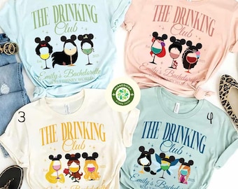 May include: Four light-colored t-shirts with a graphic design featuring Disney princesses dressed as Mickey Mouse with a glass of wine. The text on the shirts reads "The Drinking Club" and "Emily's Bachelorette Walt Disney World".
