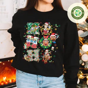 Puede incluir: Sudadera negra con un gr&aacute;fico colorido de "HO HO HO" con personajes de Toy Story con tem&aacute;tica navide&ntilde;a. El dise&ntilde;o incluye a Buzz Lightyear, Woody, Sr. Potato y otros, con detalles festivos.