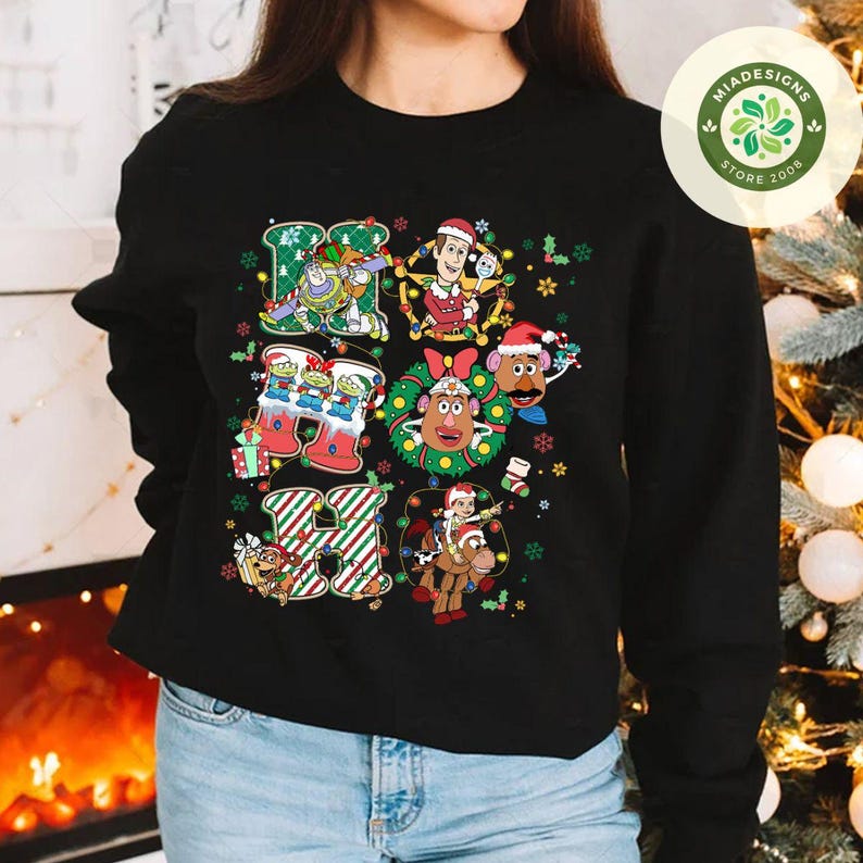 Puede incluir: Sudadera negra con un gr&aacute;fico colorido de "HO HO HO" con personajes de Toy Story con tem&aacute;tica navide&ntilde;a. El dise&ntilde;o incluye a Buzz Lightyear, Woody, Sr. Potato y otros, con detalles festivos.