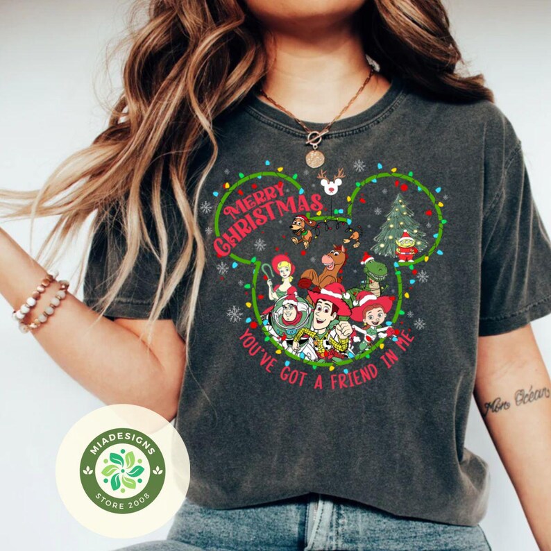 May include: Dark gray t-shirt featuring a festive design with the text "Merry Christmas" and "You've Got a Friend in Me." The design incorporates a Mickey Mouse head shape with Christmas lights and characters from the Toy Story movie.