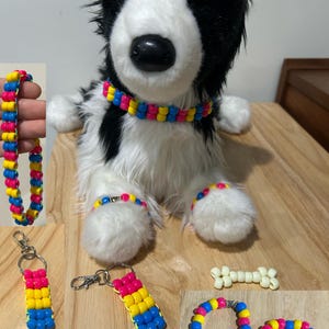 May include: A collection of accessories featuring pink, yellow, and blue plastic beads, including a collar, bracelets, and keychains. A plush black and white dog toy wears the collar and two bracelets. Two white bone-shaped bead charms are included.
