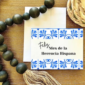 May include: A white card with blue and white tile pattern border. The card says "Feliz Mes de la Herencia Hispana".