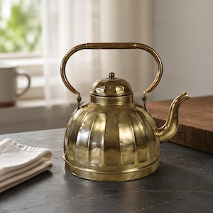 May include: A vintage-style brass kettle with a wooden handle. The kettle has a rounded body with vertical ridges and a curved spout. The handle arches over the top, and the lid has a small knob. The kettle sits on a dark countertop.
