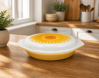 May include: A round, yellow casserole dish with a matching white lid featuring a vibrant yellow sunflower pattern on top. The dish has integrated side handles and a smooth, glossy finish, presenting a functional kitchen item for food preparation.