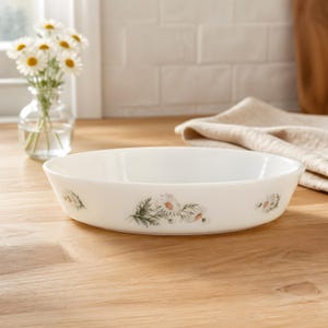 May include: A white oval serving dish with a floral daisy design. The dish is made of ceramic and has a smooth surface. The daisy design features white petals and yellow centers with green leaves.