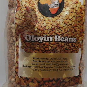 May include: A clear plastic bag filled with Oloyin Beans. The bag has a label with the text "Oloyin Beans" and a logo. The label also includes the producer and distributor information.
