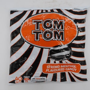 May include: A bag of Tom Tom strong menthol flavored candy. The bag is white with black and white stripes and an orange oval with the brand name "TOM TOM". The candy is black and white.