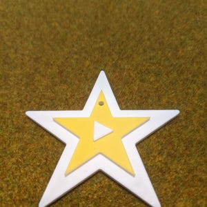 May include: A white star-shaped ornament with a yellow star inside. The yellow star has a white triangle in the center.