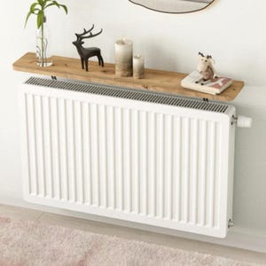 Op de afbeelding: Een witte radiator met een houten plank erboven gemonteerd. De plank is versierd met kaarsen, een hertenbeeldje en een boek.