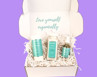 Può includere: Una scatola bianca con la scritta "Love yourself organically" sul coperchio. La scatola contiene tre prodotti: un tubo bianco con la scritta "Sprinkle" su di esso, un barattolo trasparente con la scritta "Happiness" su di esso e una bottiglia trasparente con la scritta "Soften" su di essa.