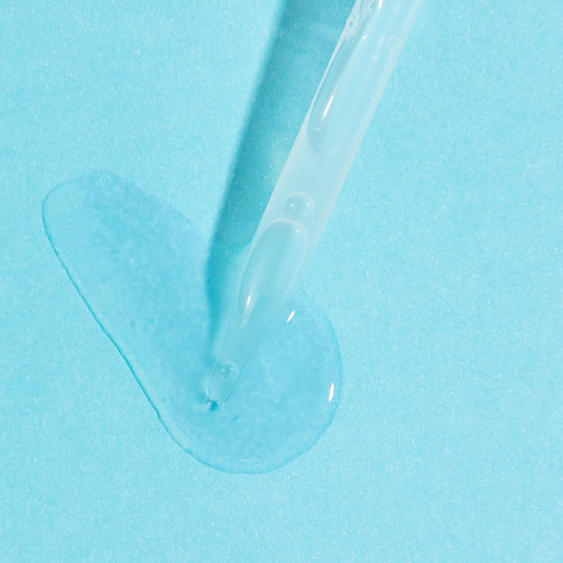 May include: A clear glass dropper bottle with a blue liquid dripping onto a light blue surface.