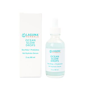 May include: A clear glass bottle with a blue liquid inside. The bottle has a white dropper top and a white label with the text "LAGUNA HERBALS OCEAN GLOW DROPS Sea Kelp + Probiotics Gel Hydrator Serum 2 oz./60 ml". The bottle is sitting on a white surface.