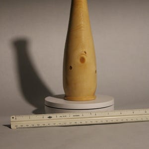 May include: A light wood vase with a narrow neck and a wide base. The vase has a natural wood grain and a few knots.