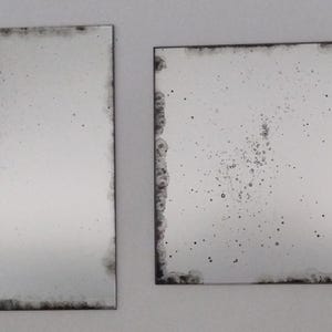 Op de afbeelding: Twee rechthoekige antieke spiegels met een verweerde zilveren afwerking. De spiegel rechts heeft meer zichtbare onvolkomenheden en een gespikkelde uitstraling.