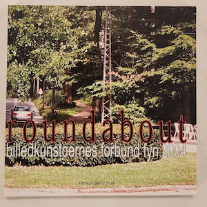 May include: A book cover with the title "roundabout" in a stylized, reddish-brown font. The background features a road with a car, trees, and a utility pole. The text "billedkunstnernes forbund fyn 2004" is also present.