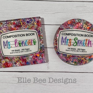 May include: Two clear resin composition book holders with colorful letter confetti inside. One holder says "Ms. Boncaro" and the other says "Mrs. Smith". Both holders have the text "100 Sheets 200 Pages 9 3/4 x 7 1/2 in/24.7 x 29.0 cm".