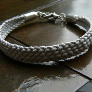 Puede incluir: Un brazalete de cuerda trenzada blanca con cierres de metal plateado.