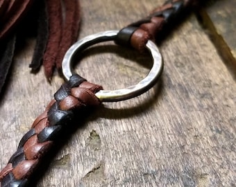 May include: A brown leather cord with a braided design and a silver ring. The cord has a fringe on one end.