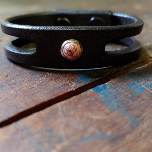 Puede incluir: Un brazalete de cuero negro con un dise&ntilde;o de doble capa y un acento de piedra rosa.
